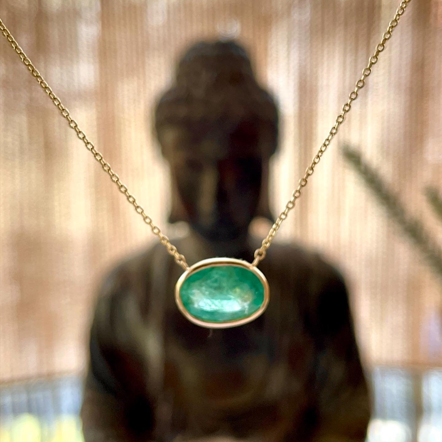 A Vedic Jyotish emerald necklace displayed in front of a Buddha statue, symbolizing spiritual healing and inner peace.